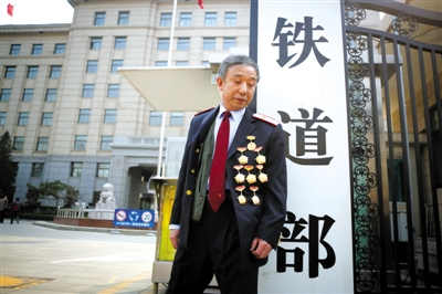 3月14日，铁道部大门口，一位胸前挂着多枚勋章的铁道部老职工与铁道部牌子合影。 新京报记者 侯少卿 摄
