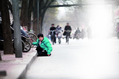 昨天下午，郑州市经三路与红旗路交叉口，一个麻将摊内，一名满头白发的老太太摸着麻将牌。不远处，一个女孩被一米多长的红绳拴住右手腕，系在马路旁的树上。