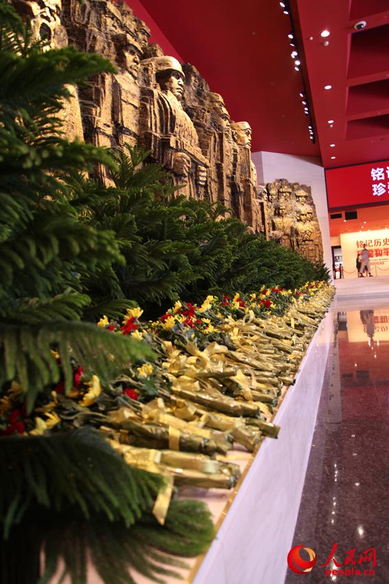 纪念馆门厅的《铜墙铁壁》雕塑墙，和人们献上的花。邱越摄